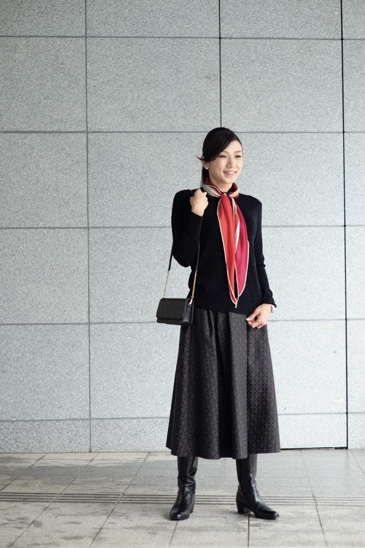 德間織恵さんが赤いスカーフを差し色にしたブラックコーデで立っている