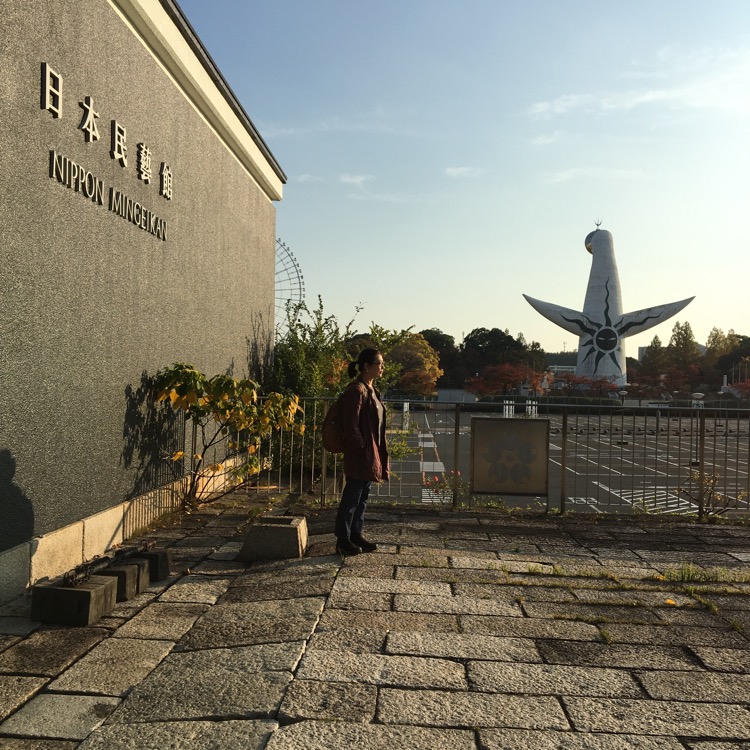 万博記念公園の太陽の塔を背景に写真を撮る石黒美穂子さん