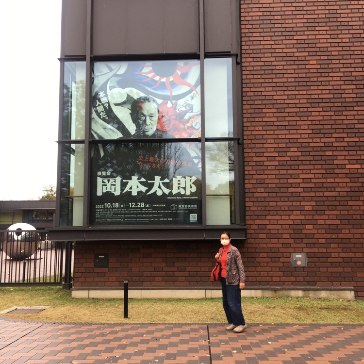 岡本太郎展の大きなポスターと並んで写真を撮る石黒美穂子さん